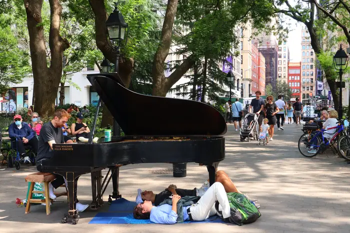 A photo of two people sitting underneath a piano in Washington Square Park